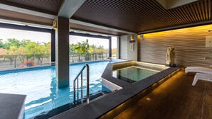 A modern indoor pool area with a clear view of the outdoors, a hot tub, and a statue. - Move Resort & Spa (Tainan)