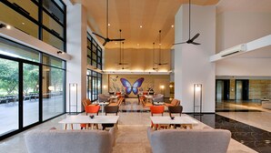 A spacious lobby with high ceilings, multiple ceiling fans, and a large butterfly mural on the wall. Tables and chairs are arranged for seating. - Tinidee Hotel Bangkok Golf Club (Pathum Thani)