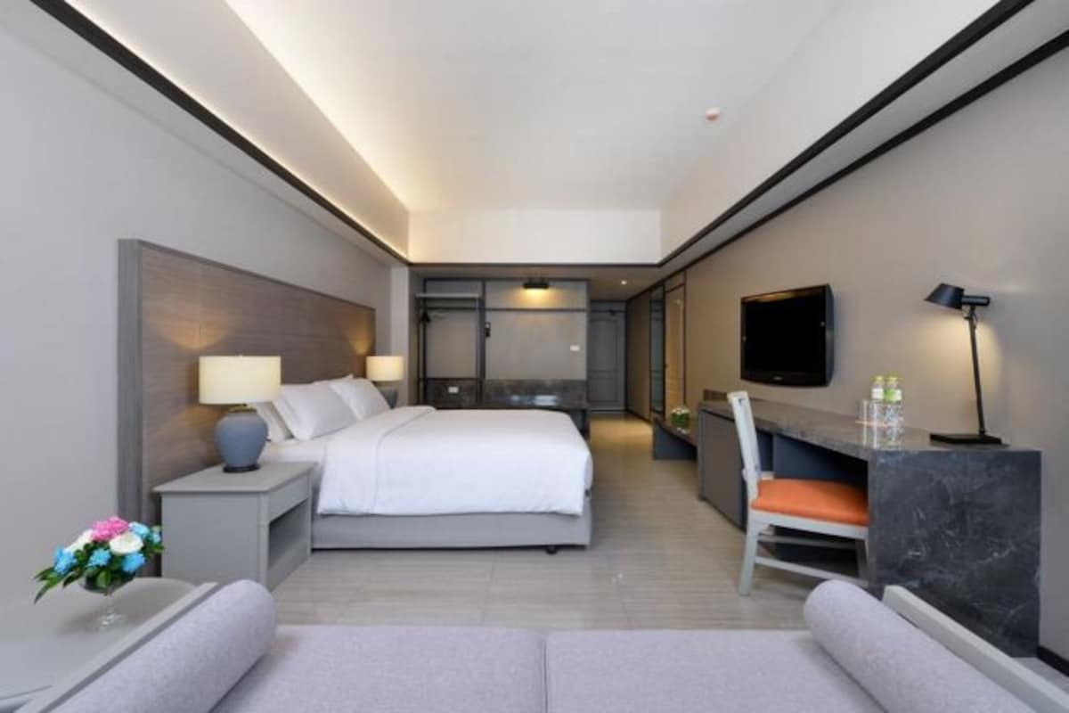 Une chambre d’hôtel moderne équipée d’un lit, d’une table de chevet, d’une lampe, d’une télévision et d’un bureau avec une chaise.