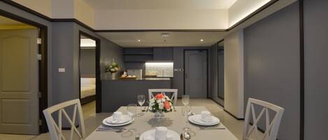 Un comedor moderno con una mesa blanca para dos, un jarrón de flores y vista a una cocina.