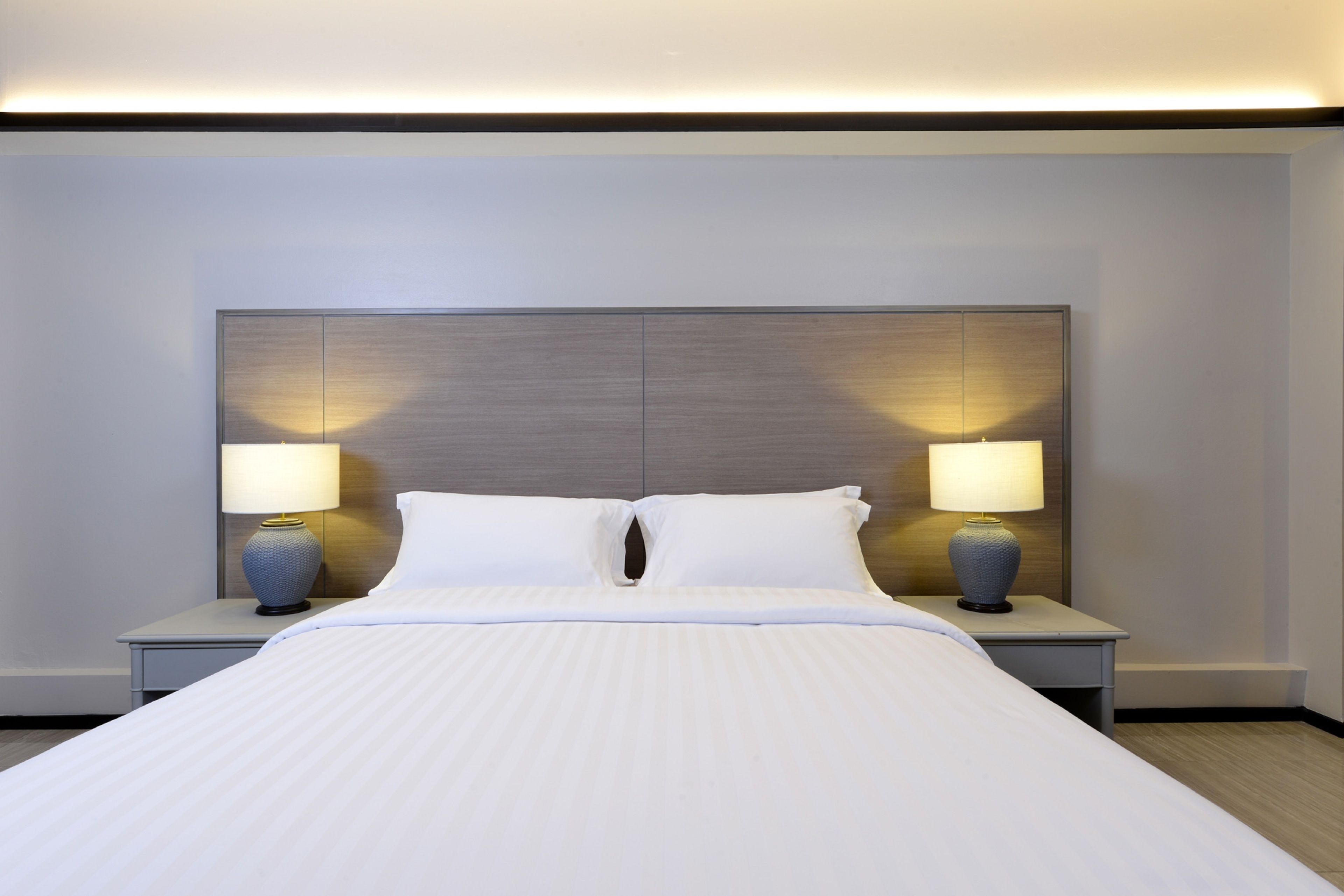 Habitación de hotel con una cama grande, dos mesitas de noche con lámparas y un cabecero moderno.