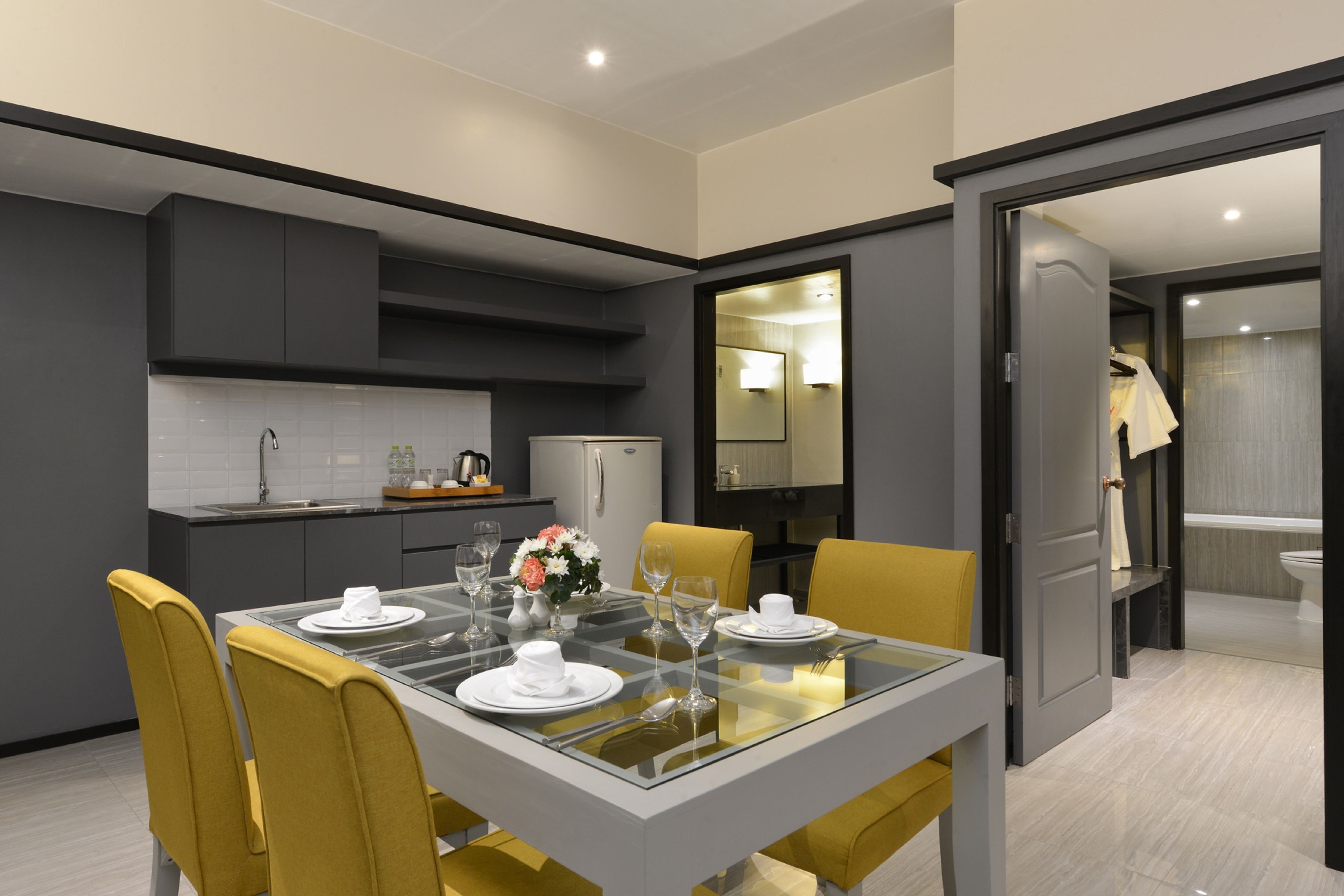 Un comedor moderno con una mesa de vidrio, sillas amarillas y una cocina al fondo.