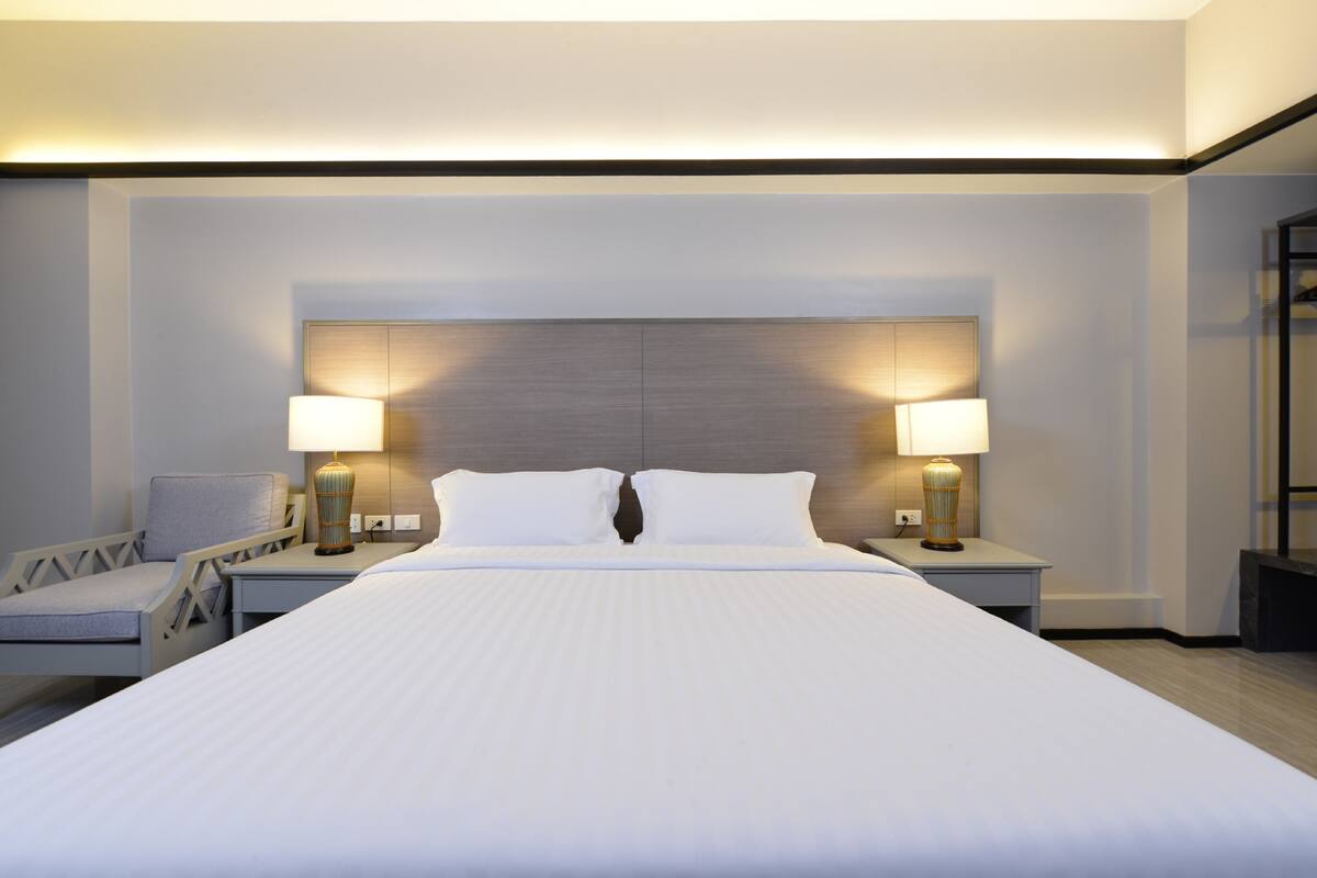 A modern hotel room with a large bed, two bedside lamps, a chair, and a nightstand.