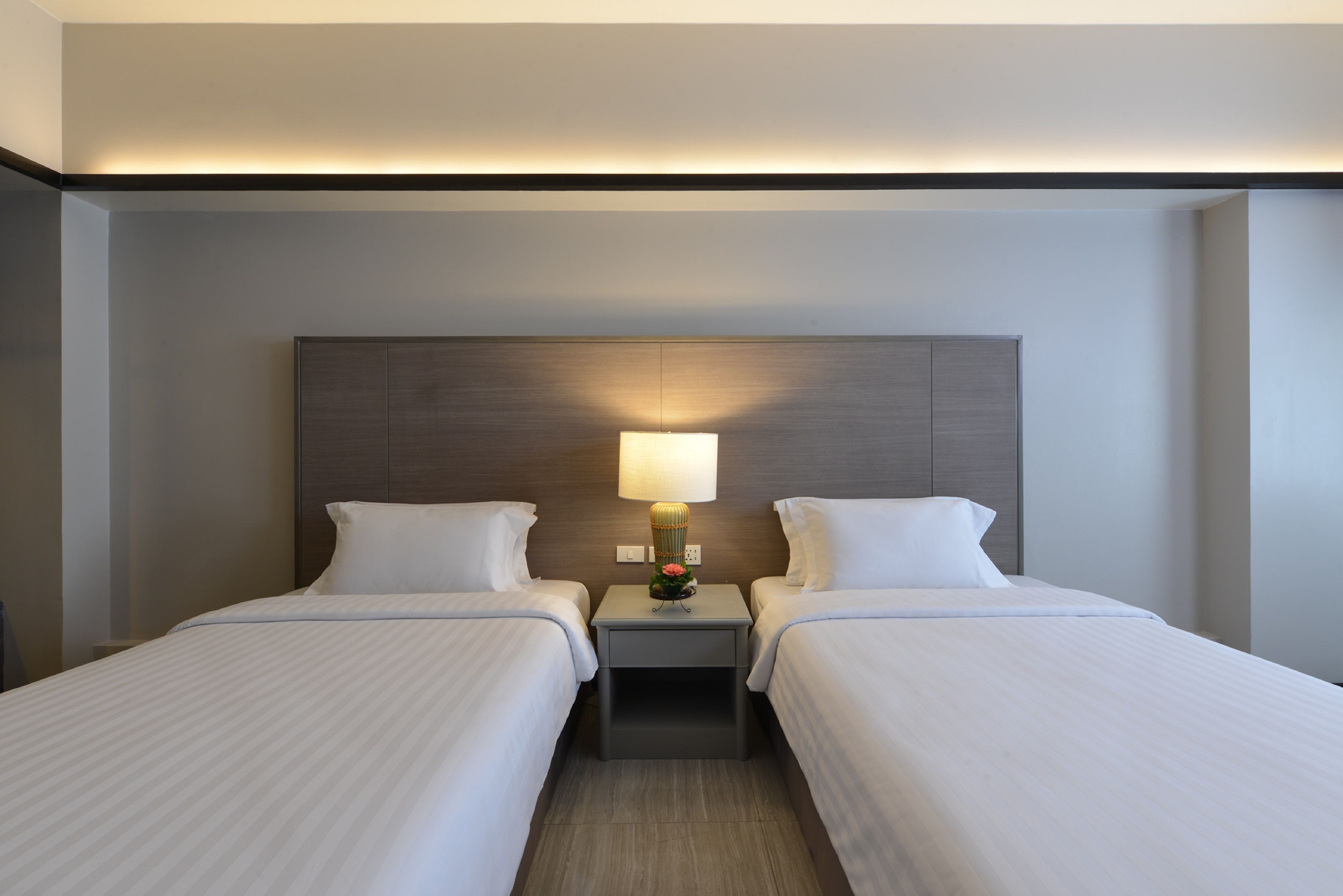 A hotel room with two beds, a nightstand with a lamp, and a wooden headboard.