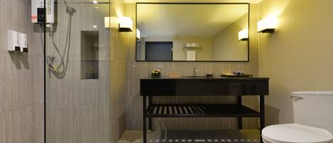 Un baño moderno con ducha envuelta en vidrio, tocador negro con espejo y un inodoro blanco.