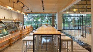 A modern interior with a long wooden table, white benches, and a glass display case with bottles. - Tinidee Hotel Bangkok Golf Club (Pathum Thani)