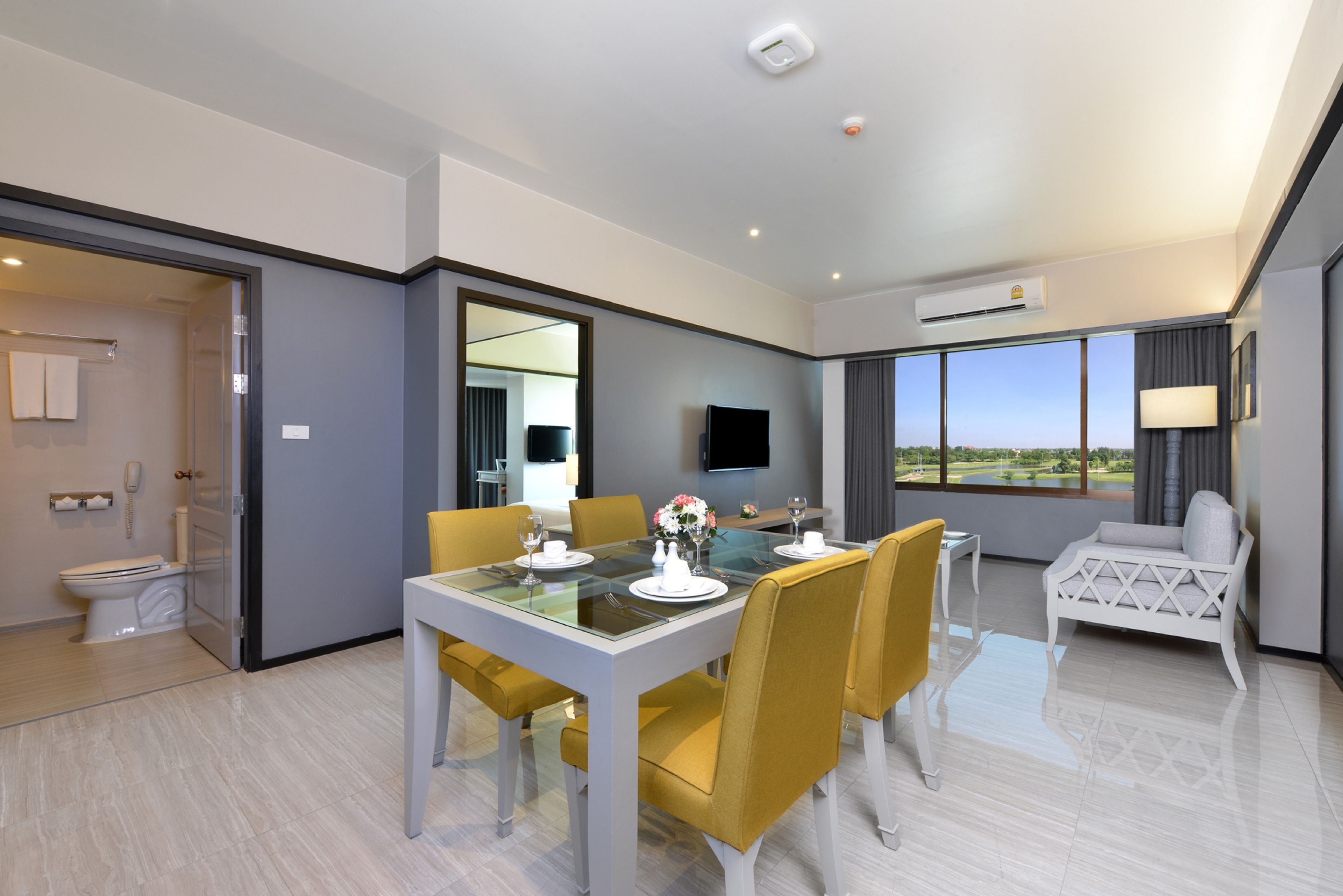 Una habitación de hotel moderna con zona de comedor, sofá, televisor y un ventanal con vistas.