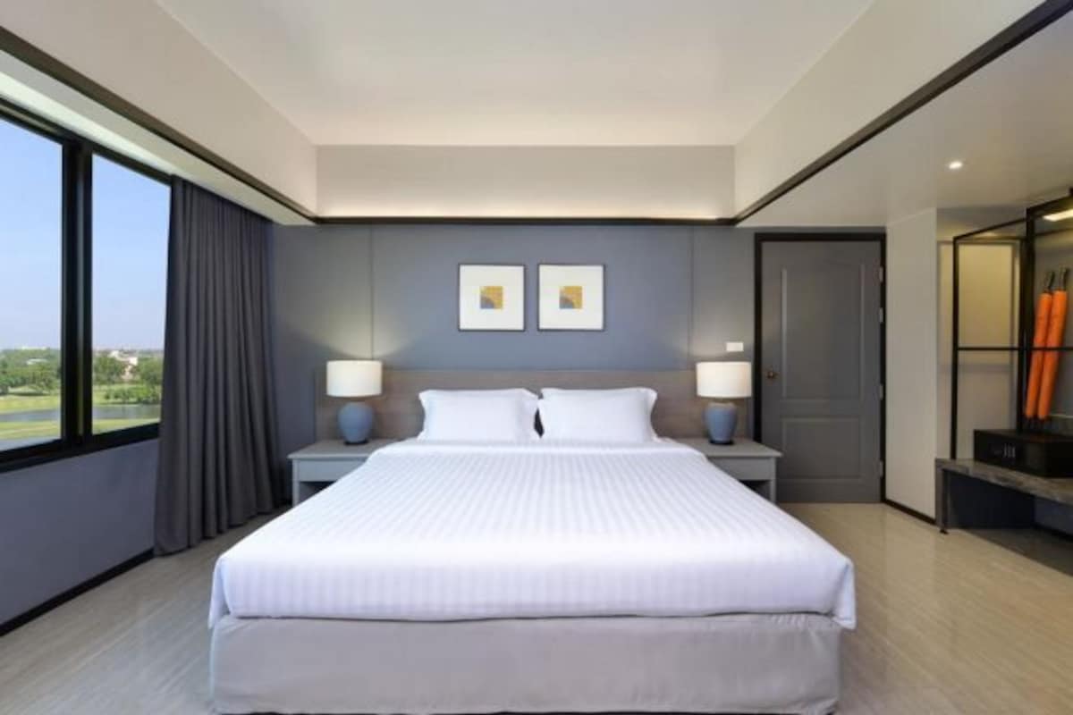 Une chambre d’hôtel moderne dotée d’un grand lit, de deux tables de chevet avec des lampes, d’une vue sur l’extérieur grâce à de grandes fenêtres et d’une porte donnant sur un balcon.
