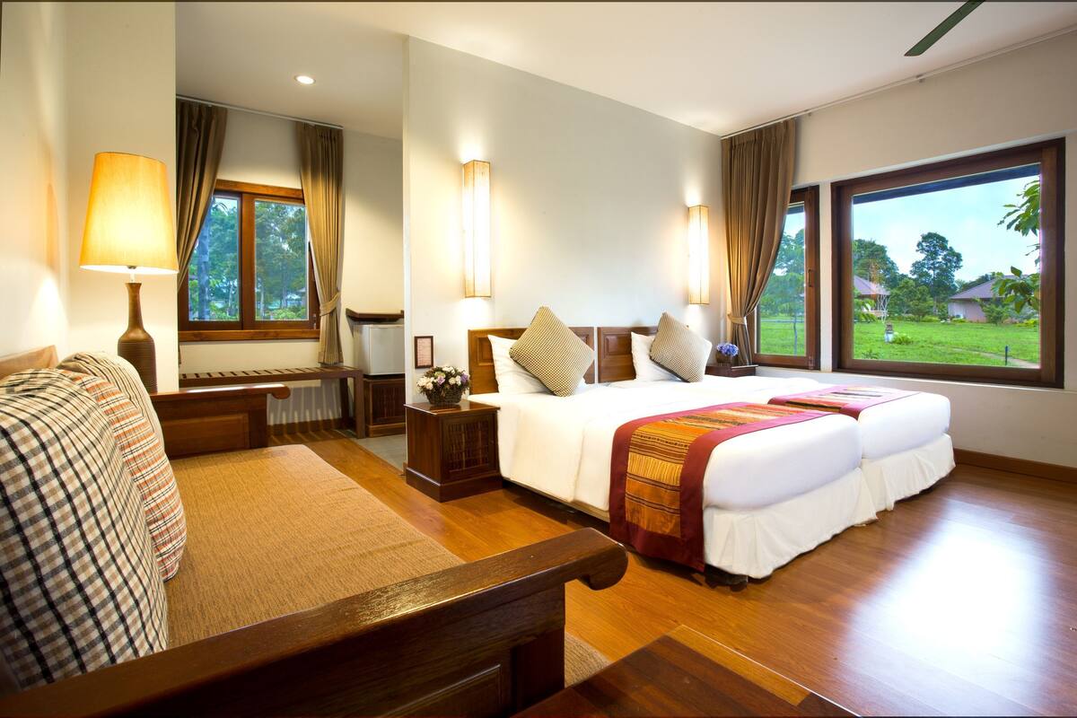 Ein Hotelzimmer mit Bett, Schreibtisch, Stuhl, Lampe und einem Fenster mit Gartenblick.