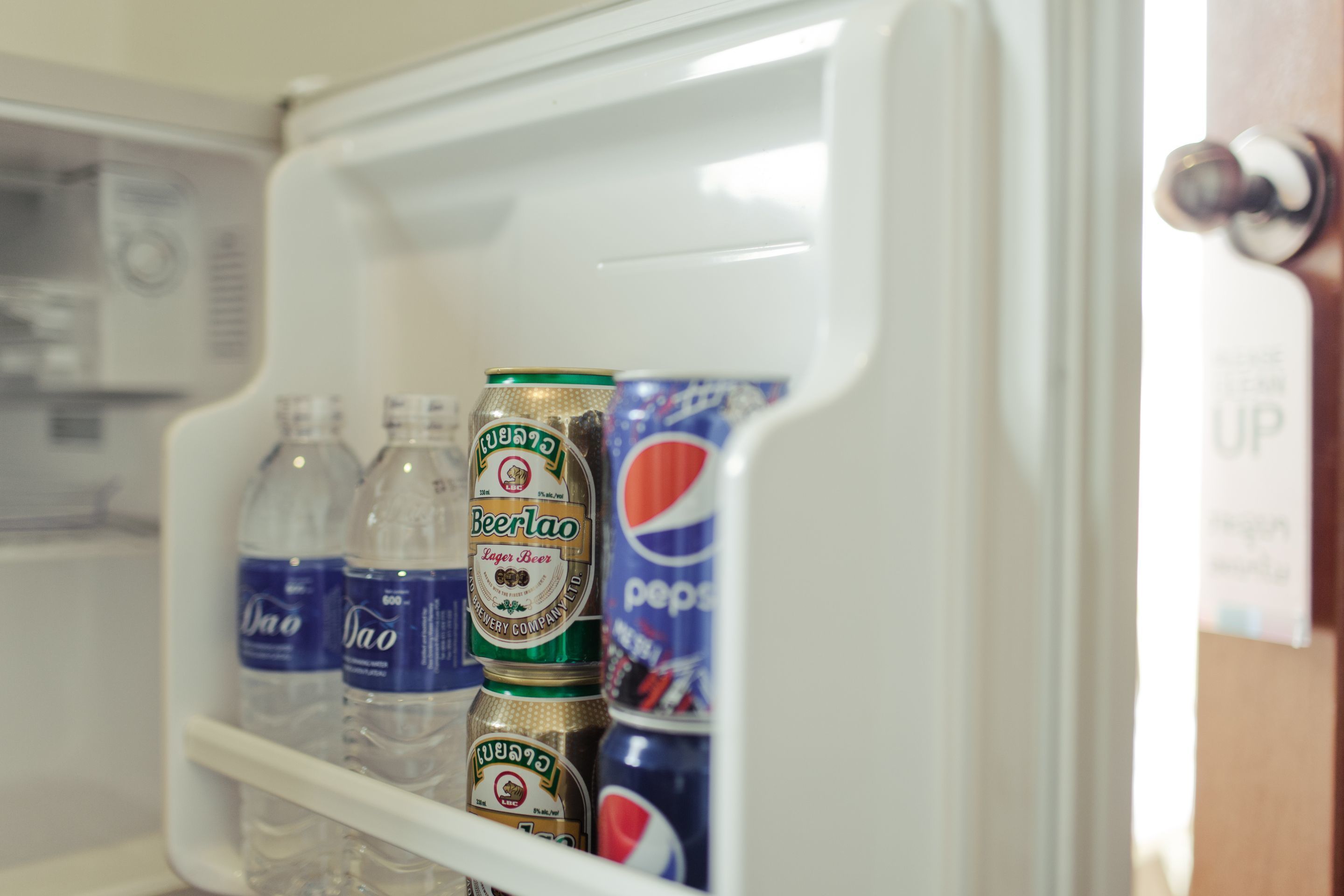 A refrigerator with water bottles, beer cans, and a Pepsi can.