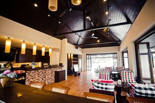 Un espacio interior amplio con techo alto, vigas de madera y una zona de estar con cojines a cuadros.