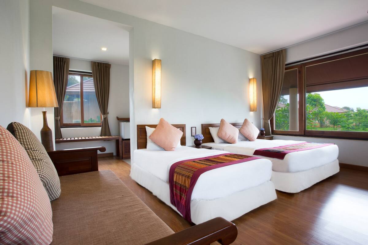 Ein Hotelzimmer mit zwei Betten, einer Couch, einem Schreibtisch und einem großen Fenster mit Vorhängen.
