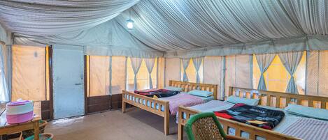 A tent-style room with three wooden beds, a wicker chair, and a table with a pink container.