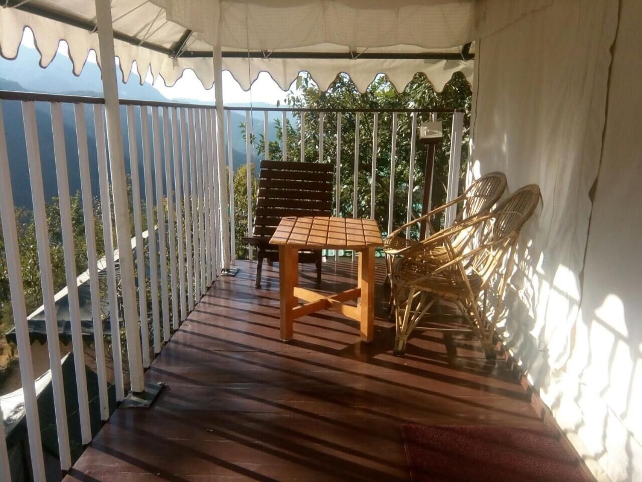 Un balcon abrité, doté d’une table et de chaises en bois, d’une balustrade et offrant une vue sur la verdure et les montagnes.