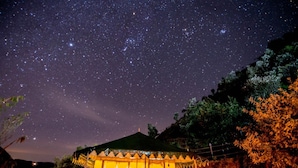 A starry night sky with a small, illuminated structure that appears to be a tent or yurt. - Nature Drops (Kosiyakutoli)