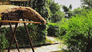 A rustic outdoor area with a thatched structure, a stone pathway, and lush greenery. - Nature Drops (Kosiyakutoli)