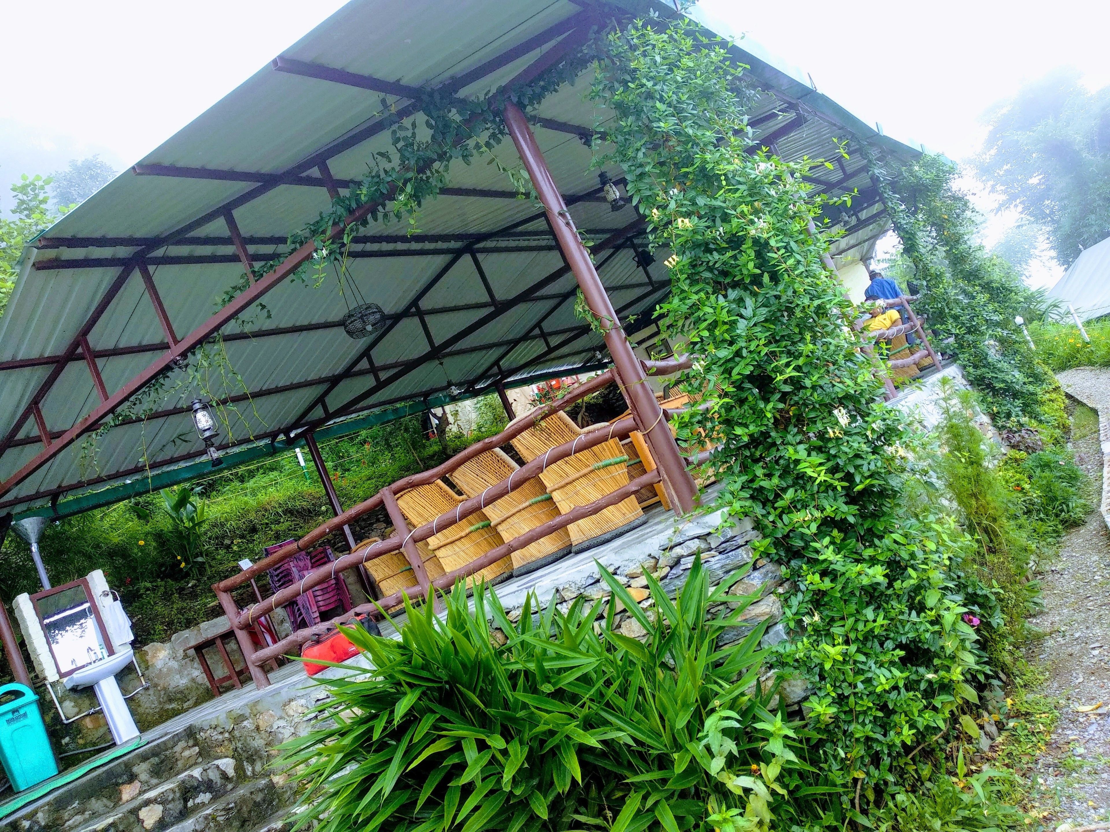 A covered seating area with bamboo furniture, a stone wall, and lush greenery.