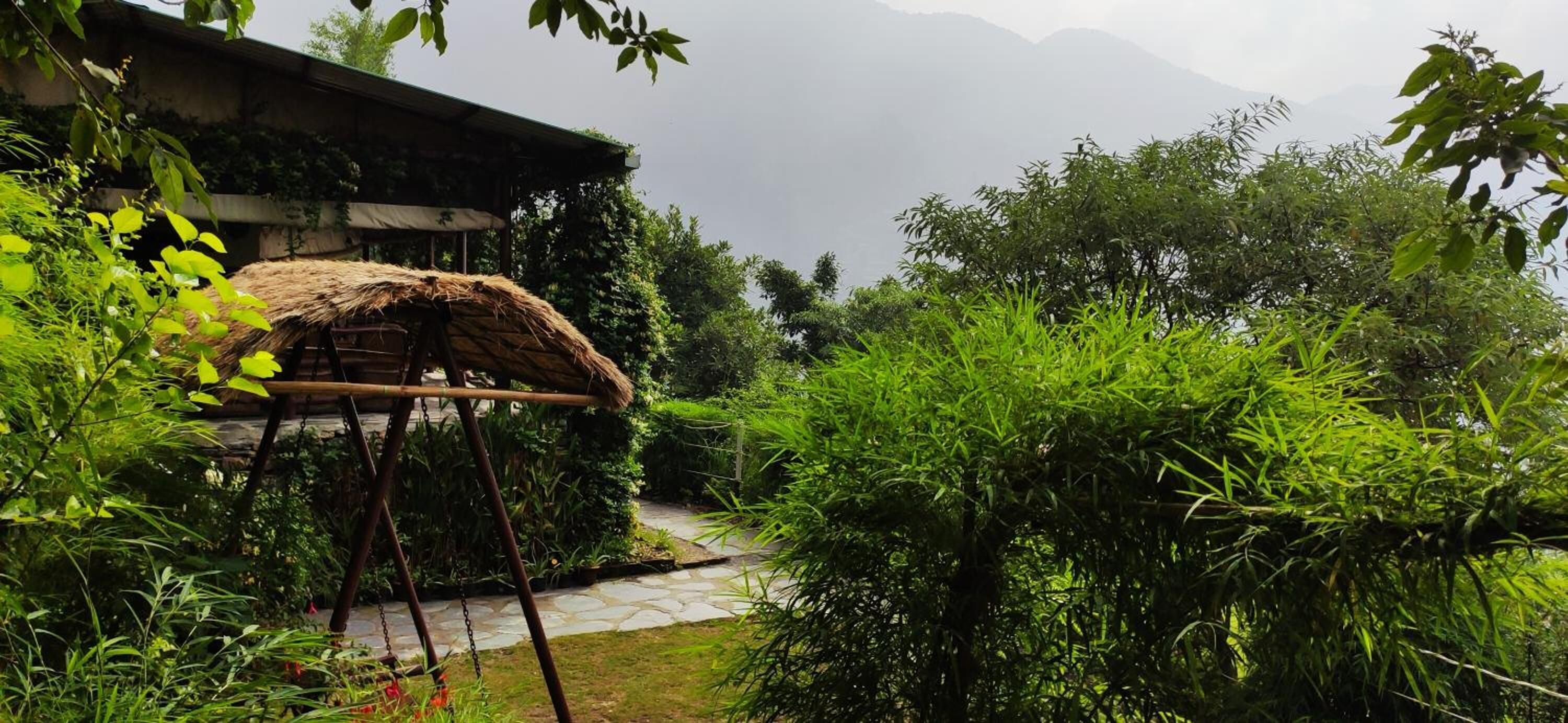 A rustic thatched-roof structure with a stone pathway leading to a mountain backdrop.