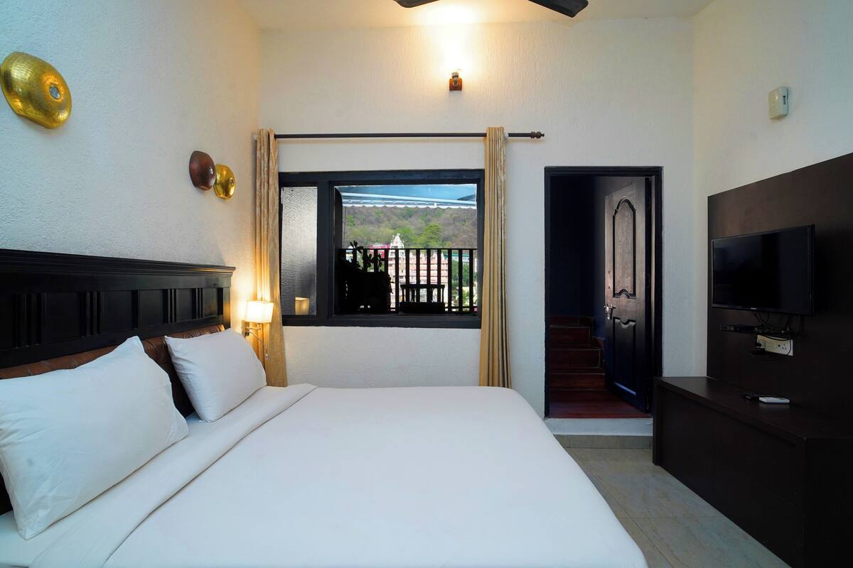 A hotel room with a bed, a TV, a window with a view, and a staircase leading to an outdoor area.