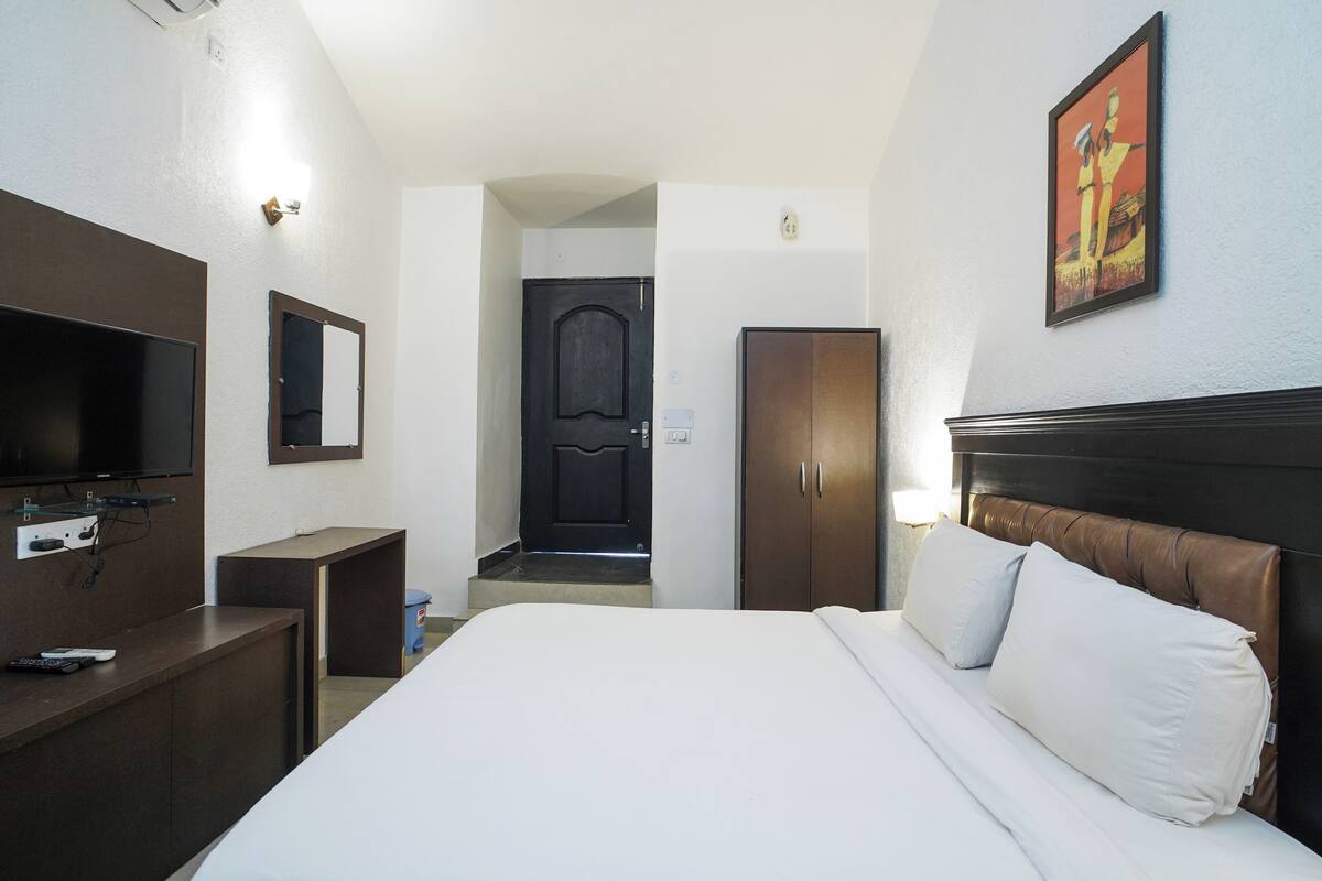 A hotel room with a bed, a TV, a desk, a wardrobe, and a door leading to another room.