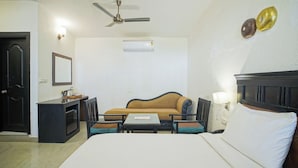 A hotel room with a bed, a sofa, a desk, a chair, a ceiling fan, an air conditioning unit, and a wall-mounted light fixture. - Hotel Ishan A Riverside Retreat (Narendranagar)