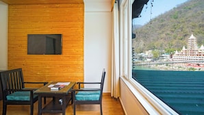 A room with a wooden ceiling, a window with a view of a temple and water, and two chairs with a table. - Hotel Ishan A Riverside Retreat (Narendranagar)