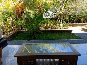 A garden area with a glass-top table, surrounded by various plants and a brick wall. - Bisma Jaya Bungalow (Ubud)