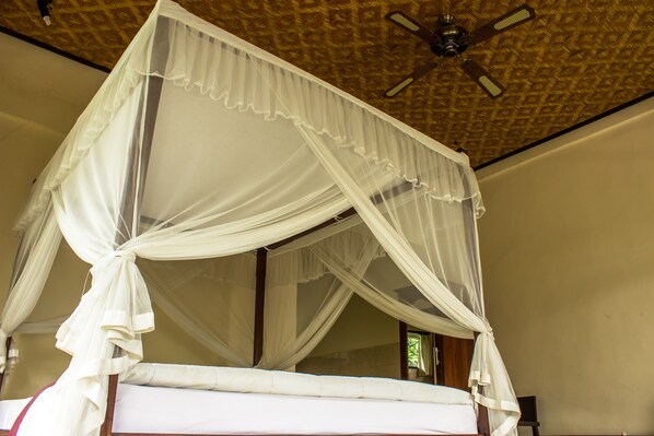 A four-poster bed with a canopy, a ceiling fan, and a window with curtains.