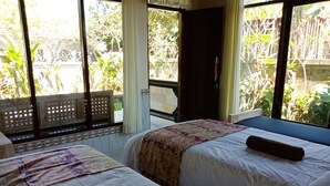 A room with two beds, a window with a view of greenery, and a door. - Bisma Jaya Bungalow (Ubud)