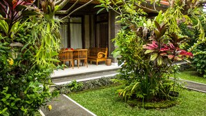 A garden with a wooden bench and chairs, surrounded by various plants and a pathway. - Bisma Jaya Bungalow (Ubud)