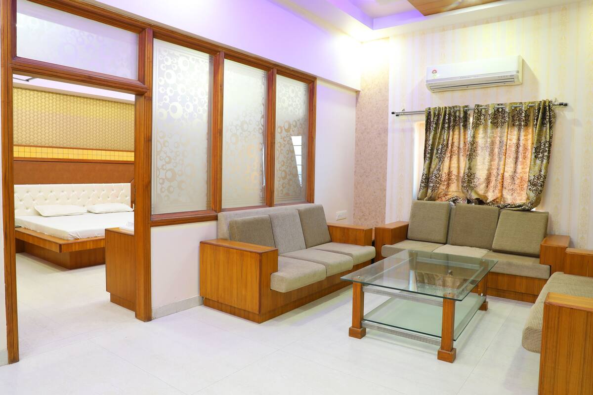 A modern living room with a sofa, a glass coffee table, and a bed with a wooden headboard.