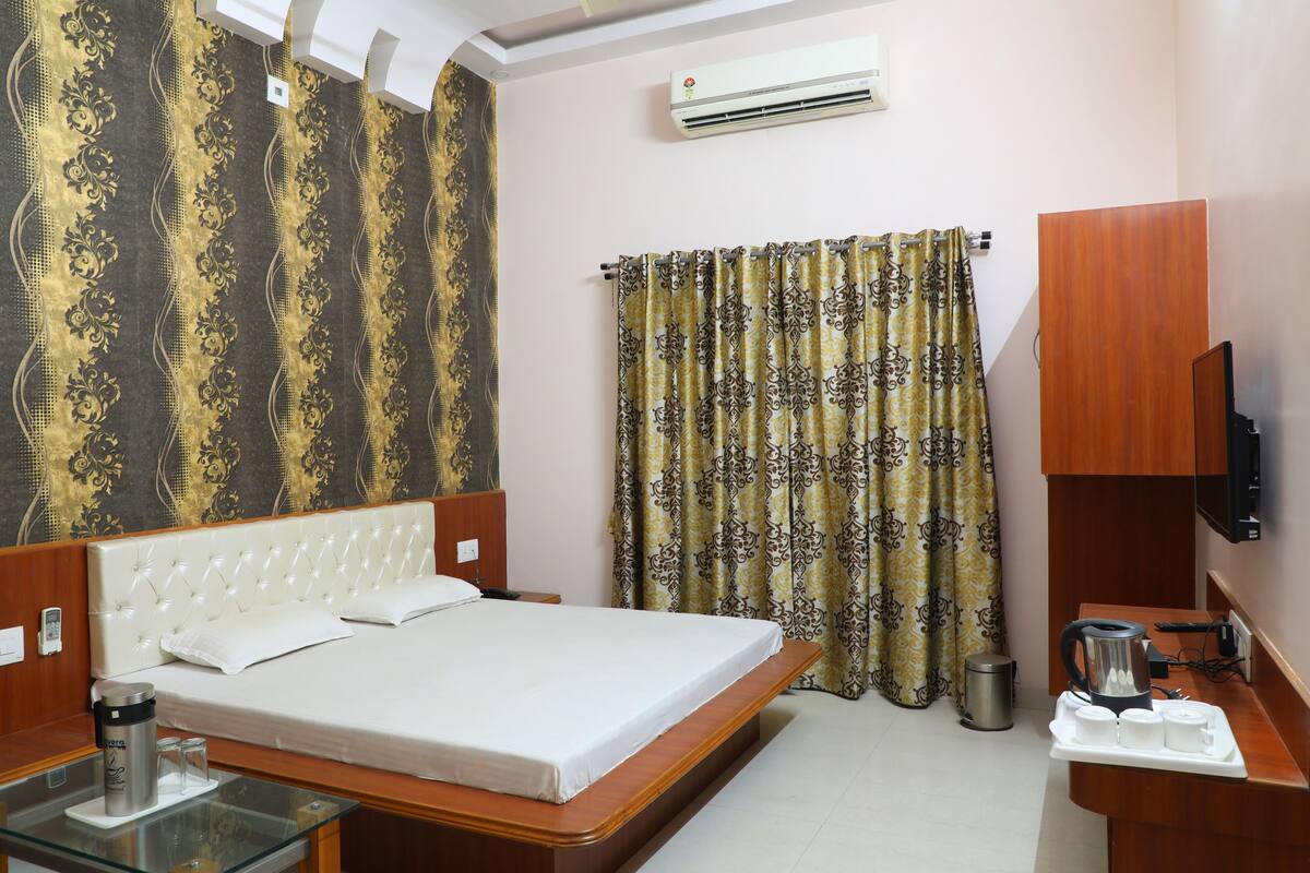 A hotel room with a large bed, a glass table with a water bottle, a coffee maker, and a TV on a wooden cabinet.