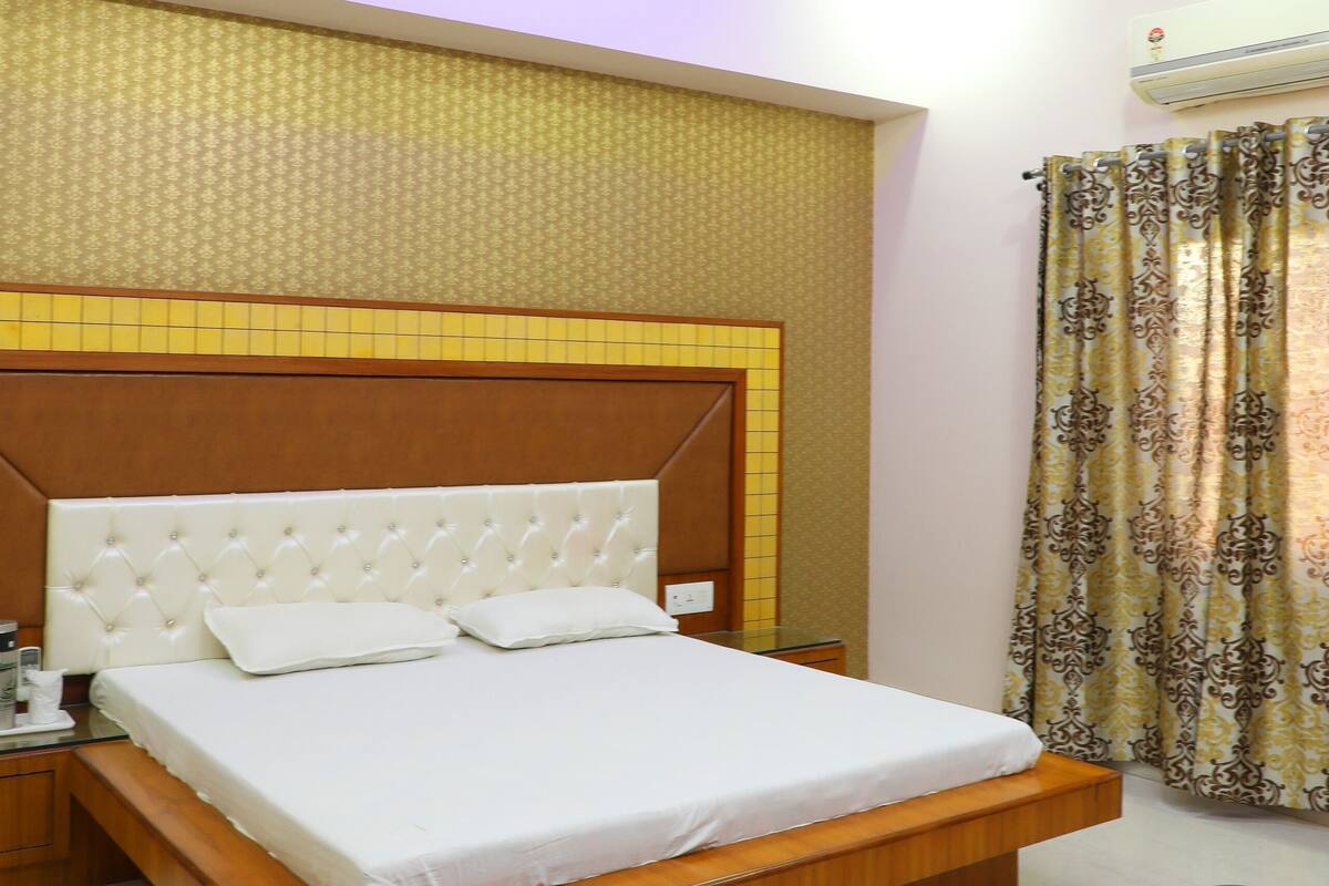 A hotel room with a bed, a ceiling fan, an air conditioning unit, and a coffee maker on the side table.