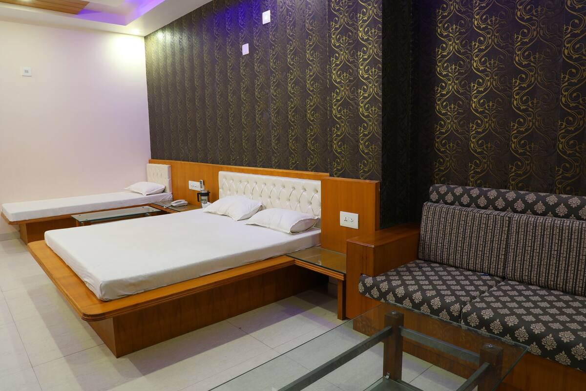 A hotel room with two single beds, a sofa, and a glass partition.