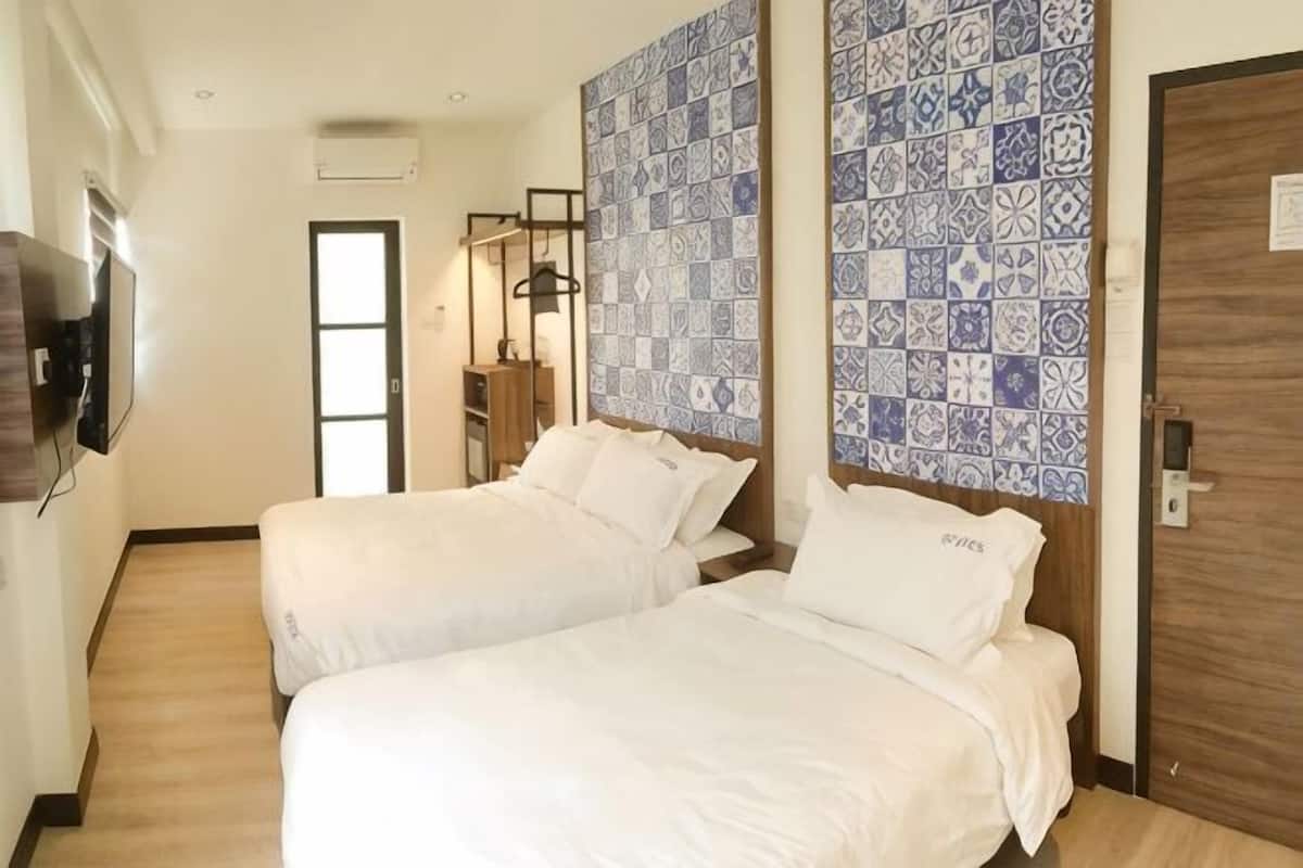 A hotel room with two beds, a TV, a wardrobe, and a patterned wall.