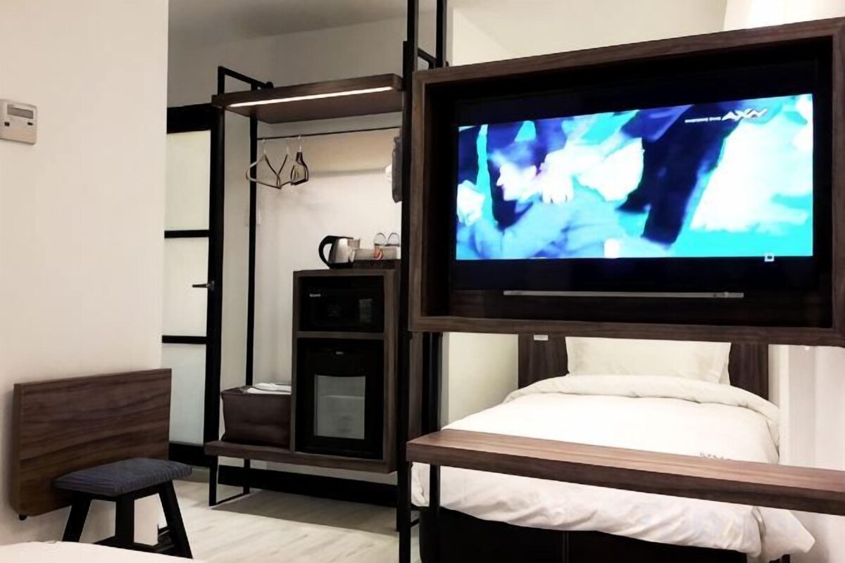 A bedroom with a bed, a TV mounted on a wall, a desk, and a chair.