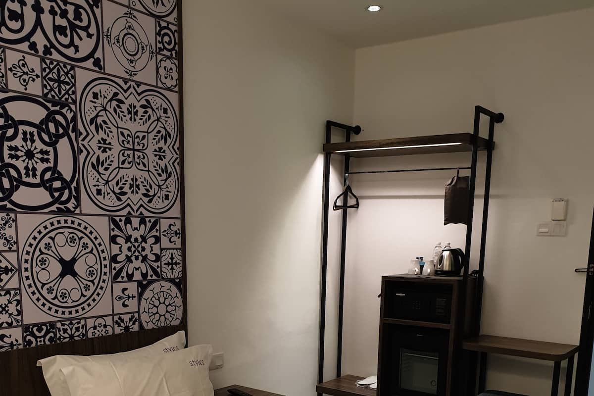 A hotel room with a bed, a bedside table, a hanging chair, a desk, and a wall with decorative tiles.