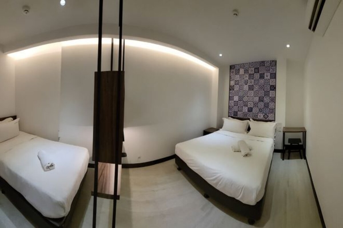 Una habitación de hotel moderna con dos camas, techo curvo y pared con estampado.