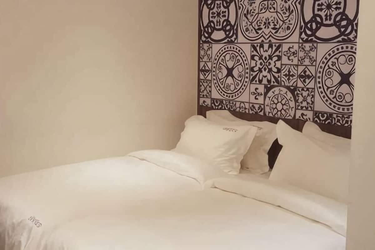 A bed with white bedding, a headboard with a patterned design, and a plain wall.