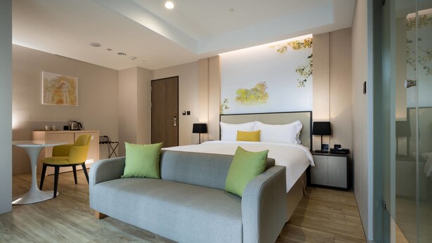 Una habitación de hotel moderna con una cama grande, un sofá, una mesita y una silla.