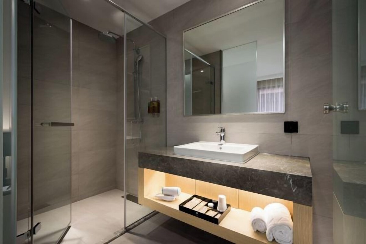 A modern bathroom with a glass-enclosed shower, a white sink, and a mirror above it.