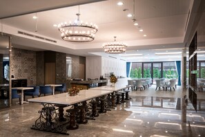 A spacious dining area with a long table, elegant chandeliers, and a view of the outdoors.