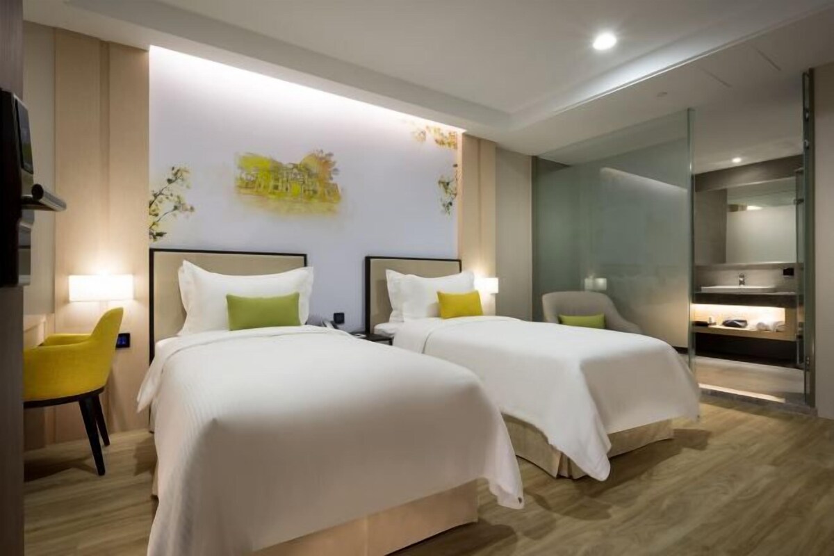 A hotel room with two beds, a yellow chair, a mirror, and a small table.