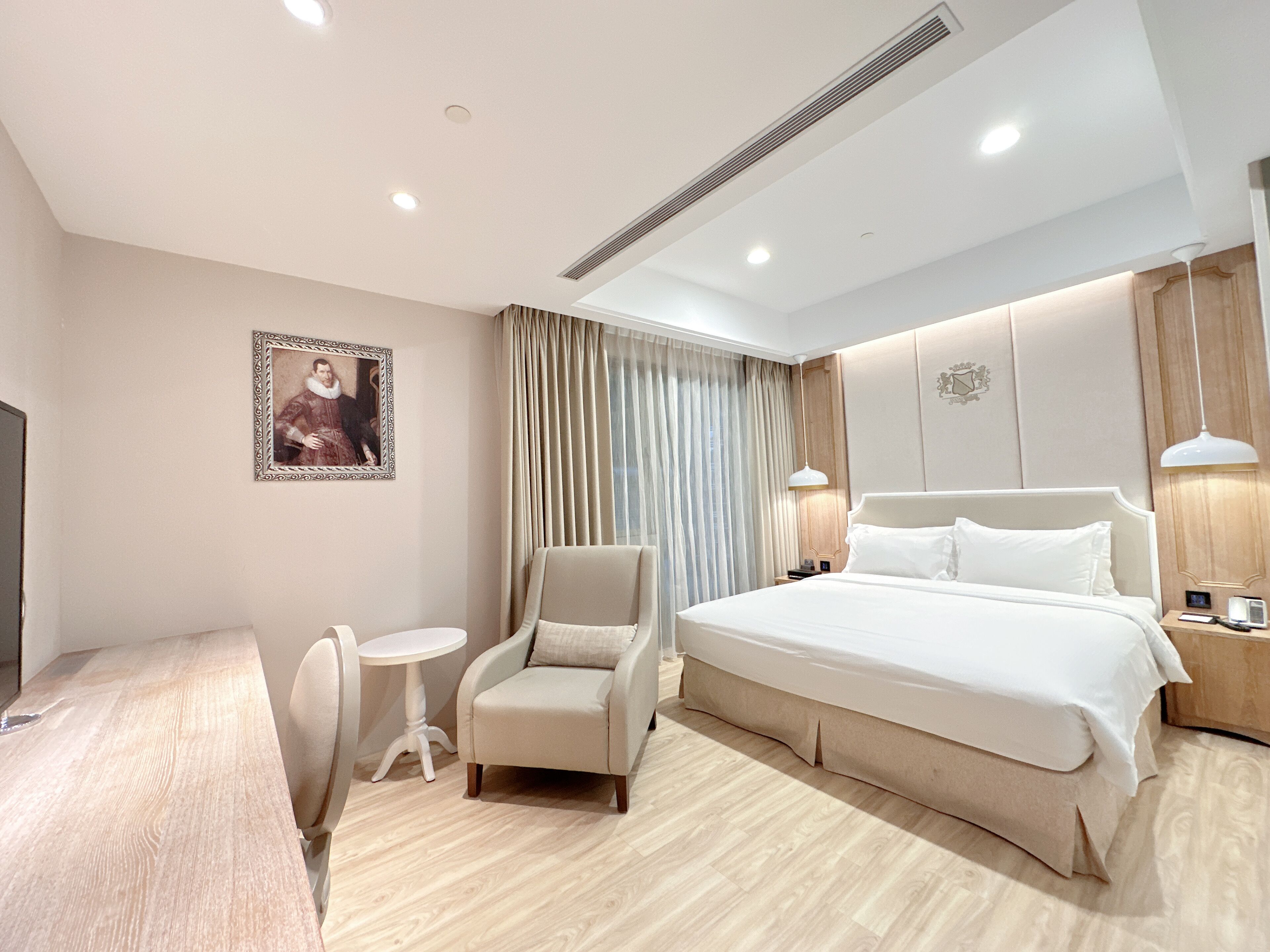 Una habitación de hotel moderna con una cama grande, un rincón de descanso con una silla y una mesa, un escritorio pequeño y un cuadro en la pared.