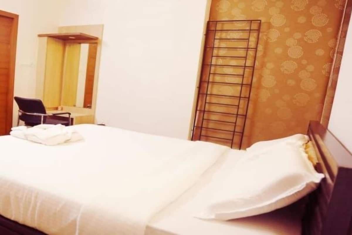 Quarto de hotel com cama, poltrona, guarda-roupa e janela com persianas.