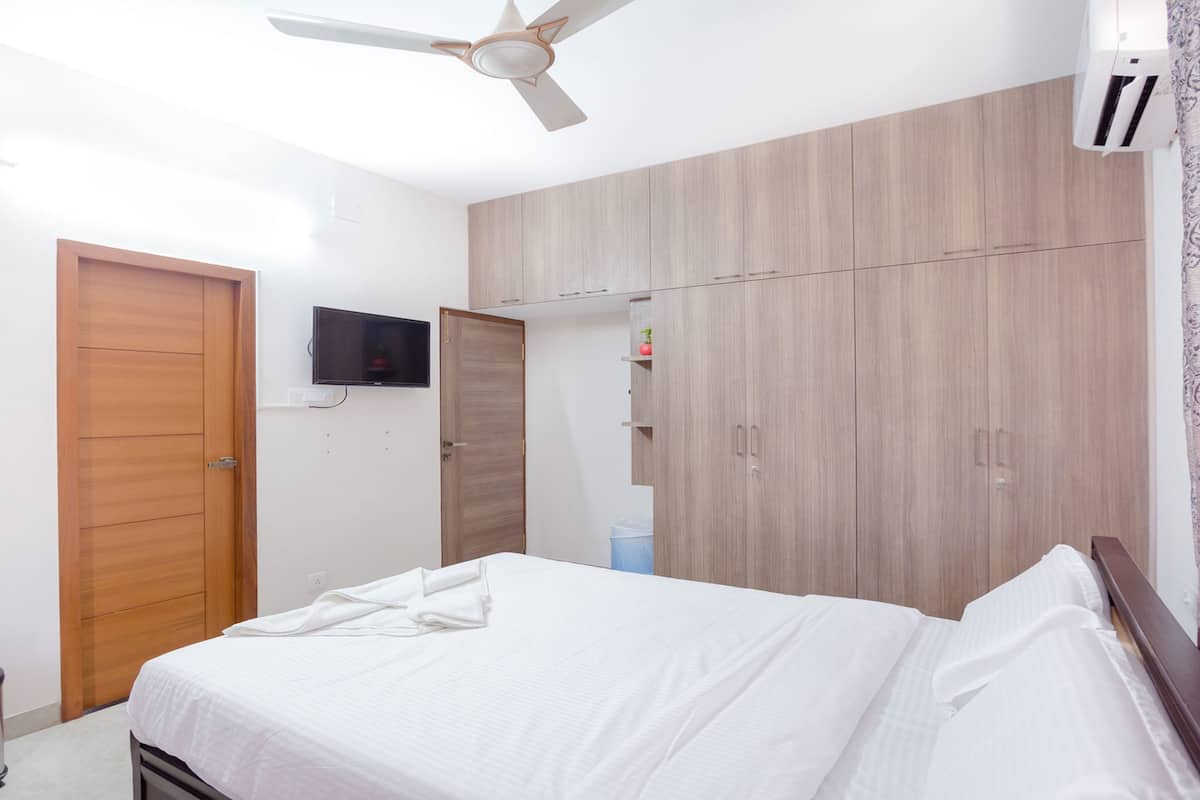 Quarto com cama, guarda-roupa de madeira, ventoinha no teto e televisão na parede.