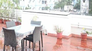 A rooftop terrace with a table and chairs, potted plants, and a view of buildings in the background. - Kolam Serviced Apartments - Adyar (Chennai)