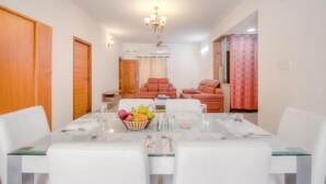 A dining area with a glass table, white chairs, a fruit bowl, and a red-striped curtain in the background. - Kolam Serviced Apartments - Adyar (Chennai)