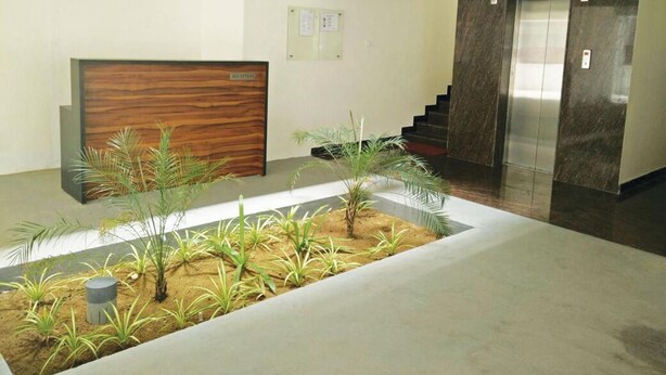 A reception area with a wooden reception desk, a small indoor garden, and an elevator. - Kolam Serviced Apartments - Adyar (Chennai)