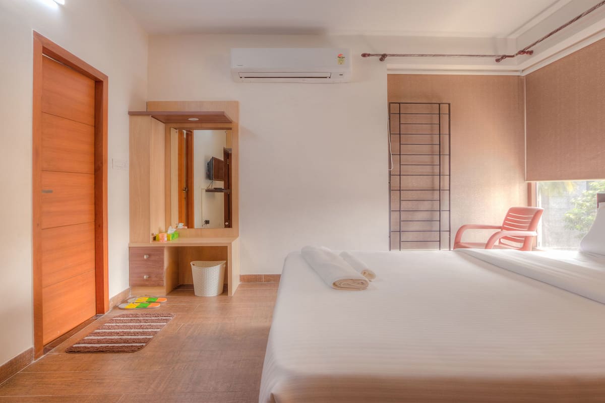 Quarto de hotel com uma cama, uma cadeira, um guarda-roupa, um espelho e uma janela.